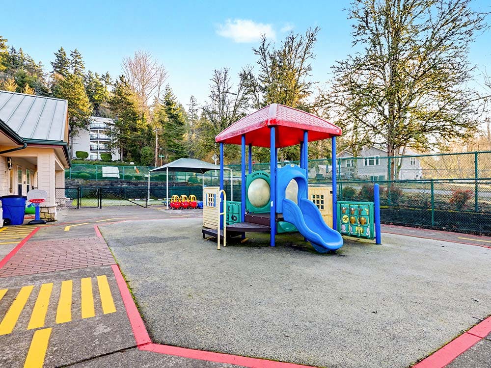 Colorful playground structure with a red roof and blue slide on a paved area