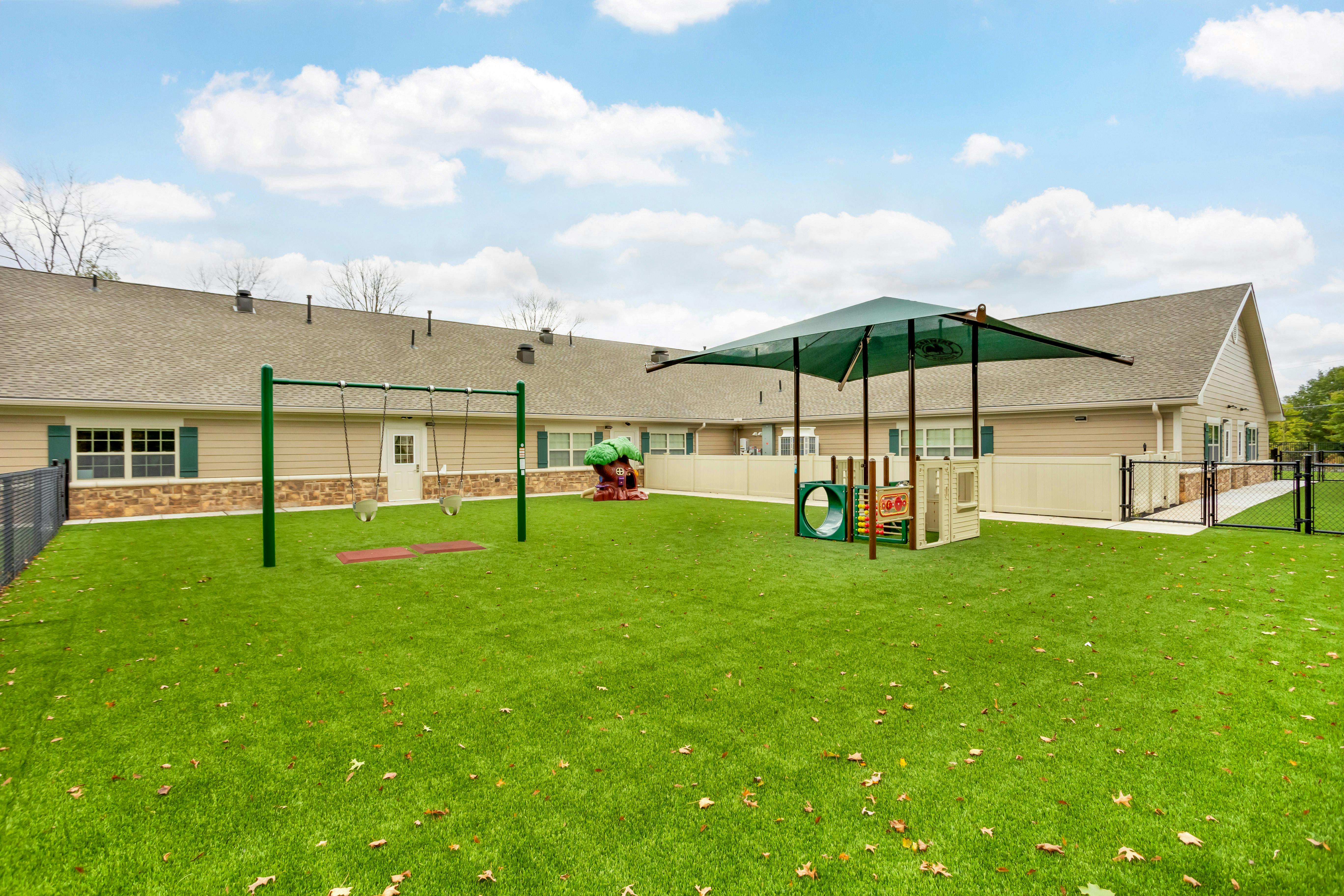Outdoor playground with swings, small play structure, and green artificial turf