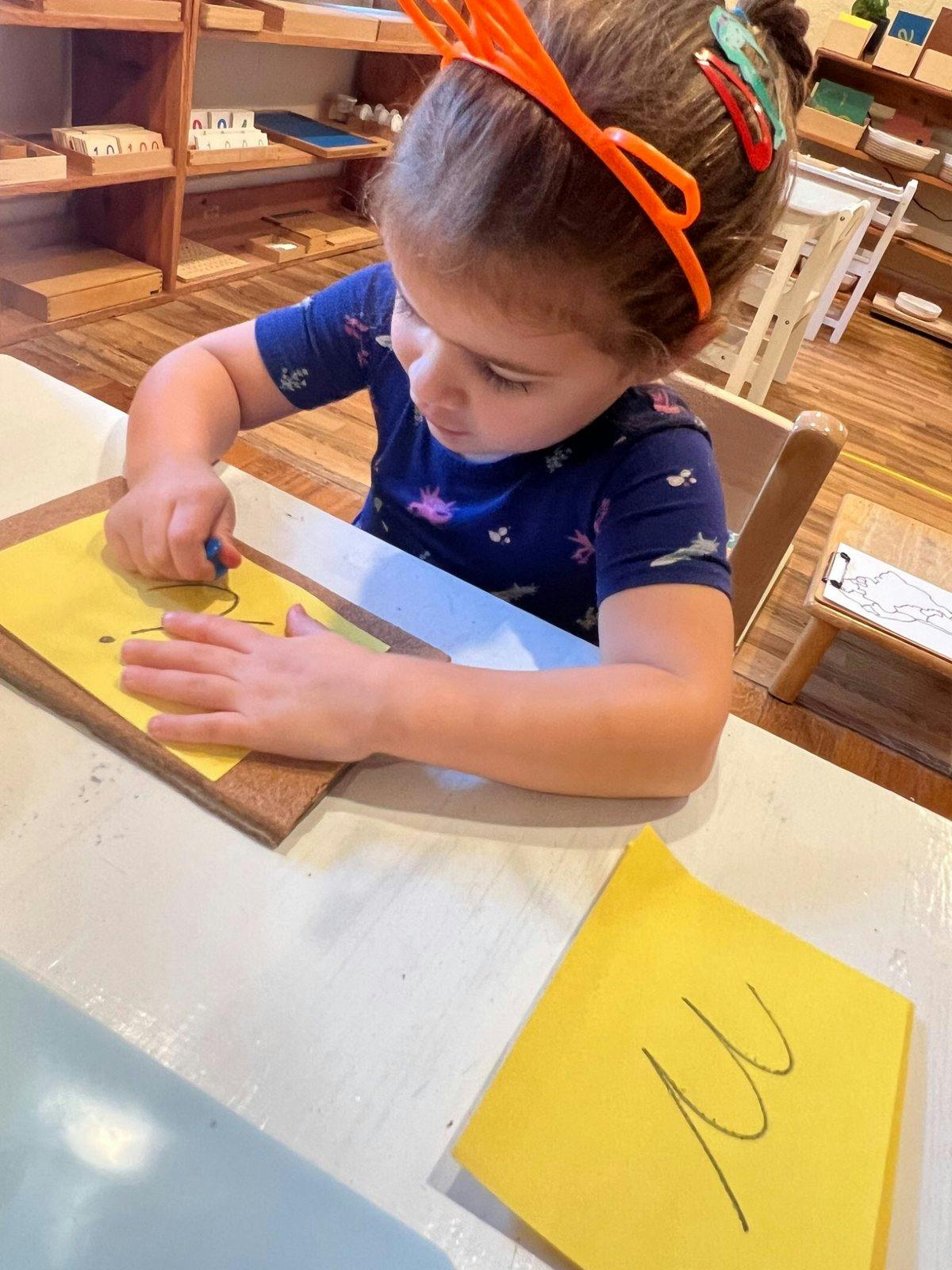 Child writing on paper at a table in a classroom