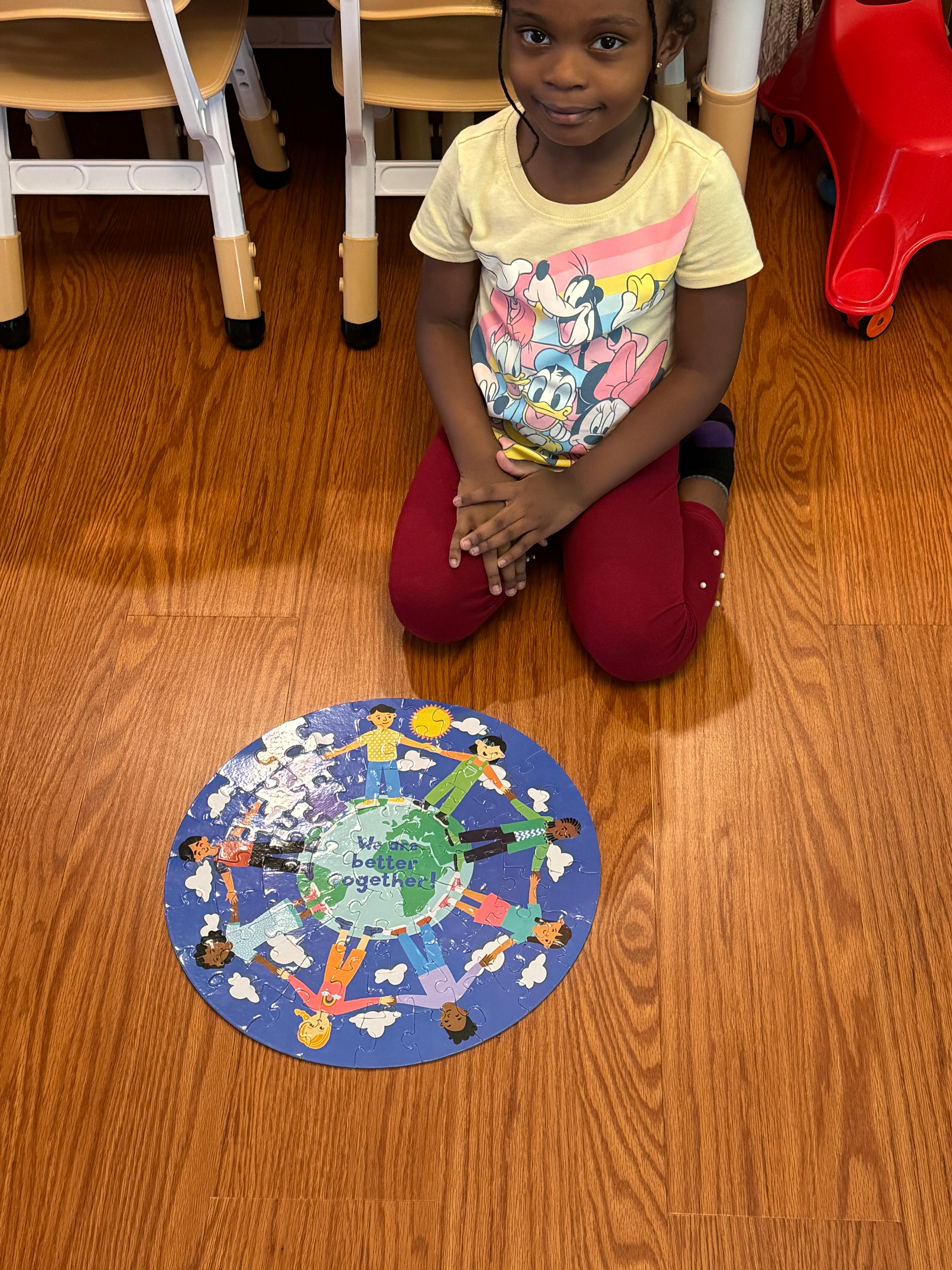 Child kneeling on floor next to a circular puzzle with people holding hands