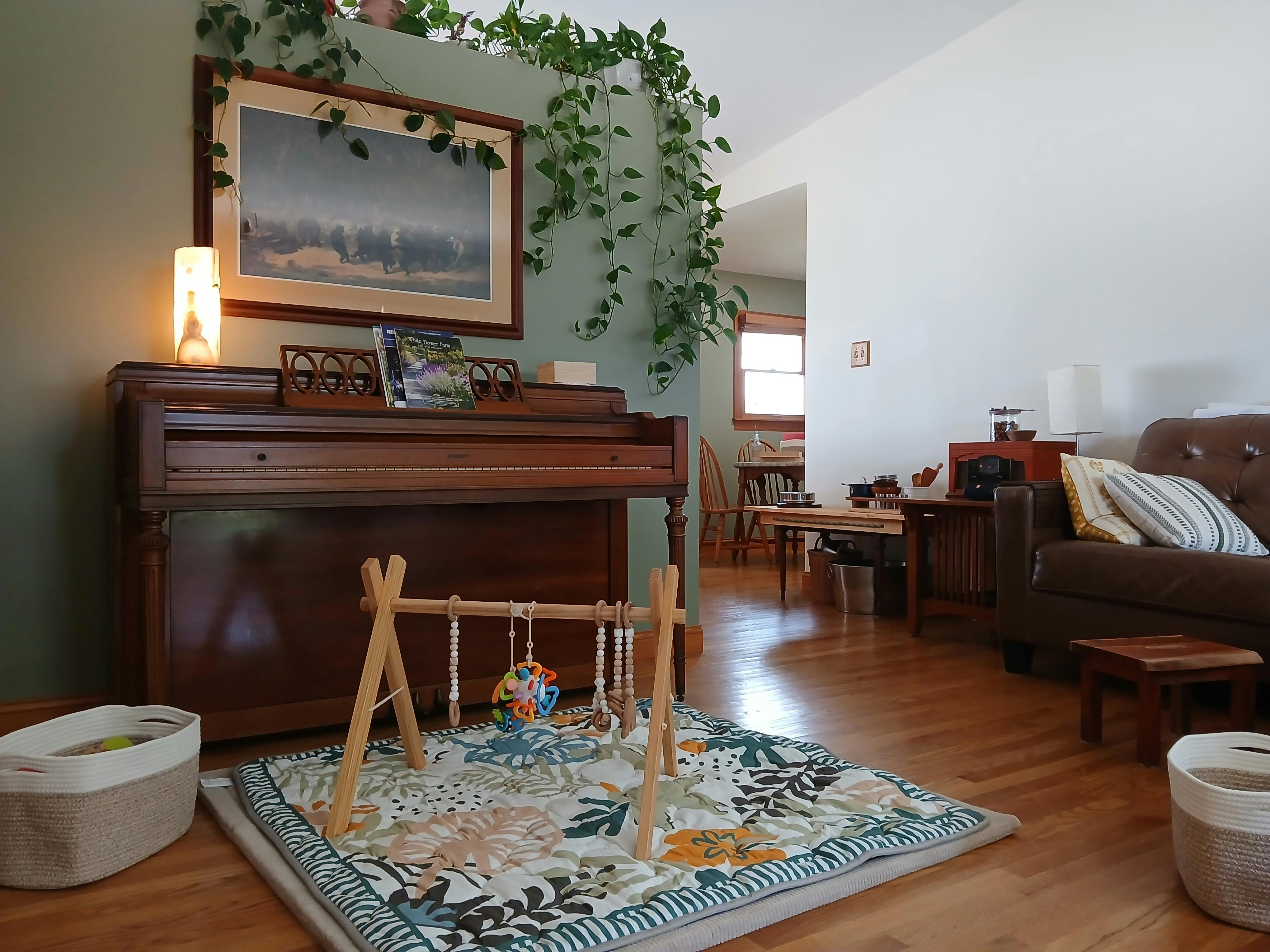 Wooden infant play gym on a patterned mat in a living room with a piano