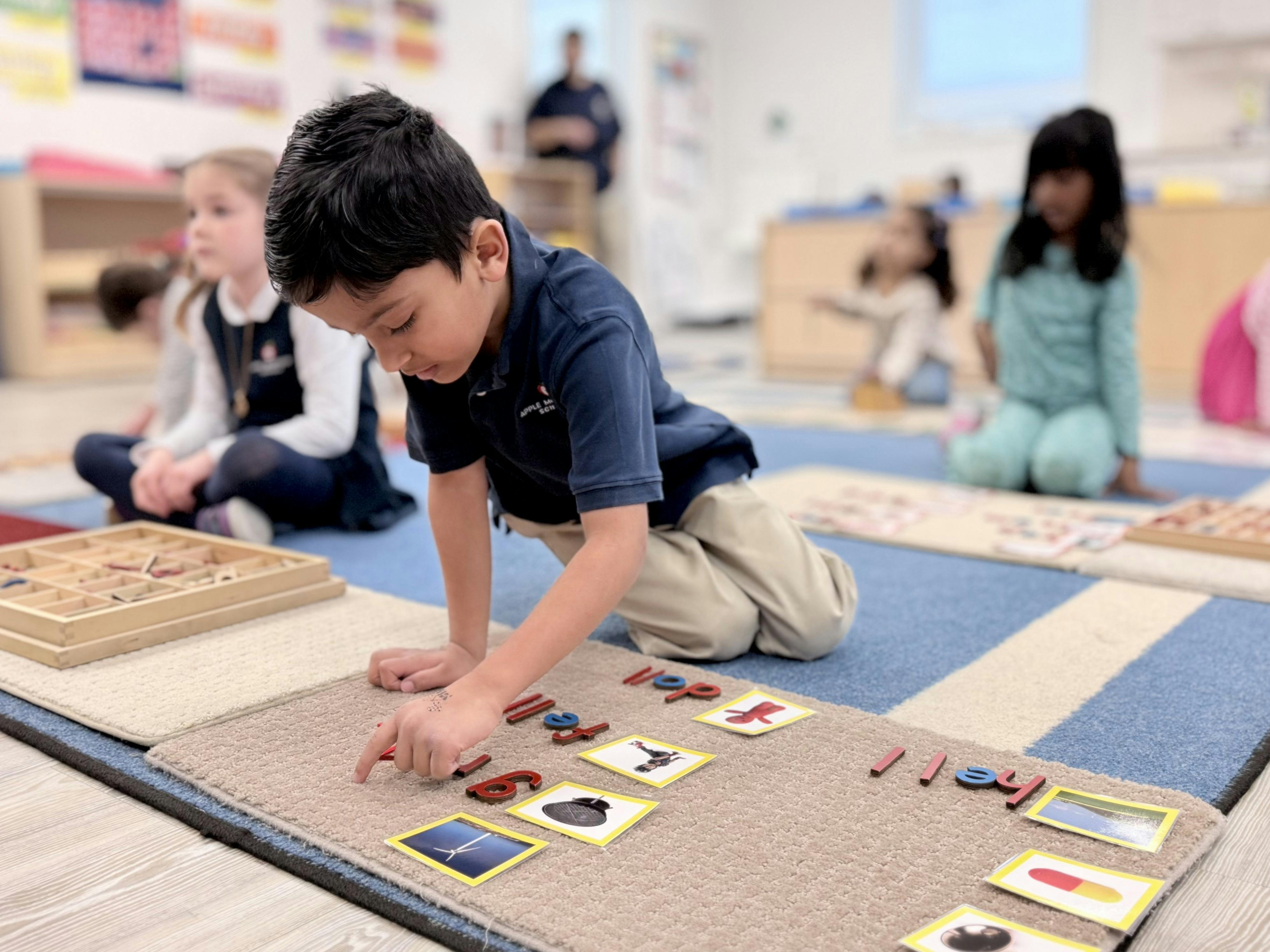Child on a classroom floor playing with letter and number tiles and picture tiles