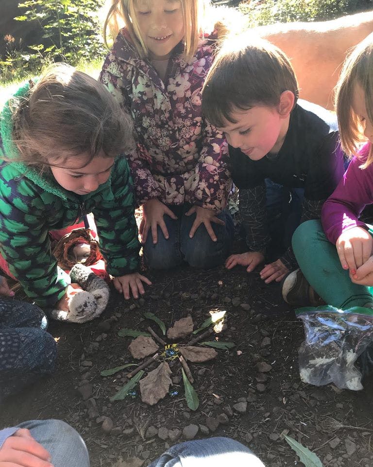 Children kneeling around a natural art piece made of leaves and sticks