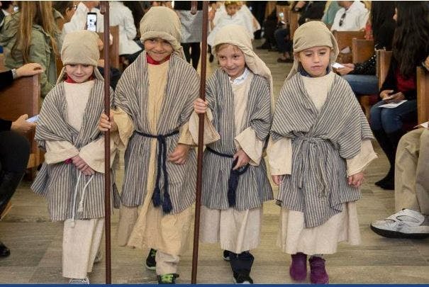Four children in robes and head coverings holding staffs