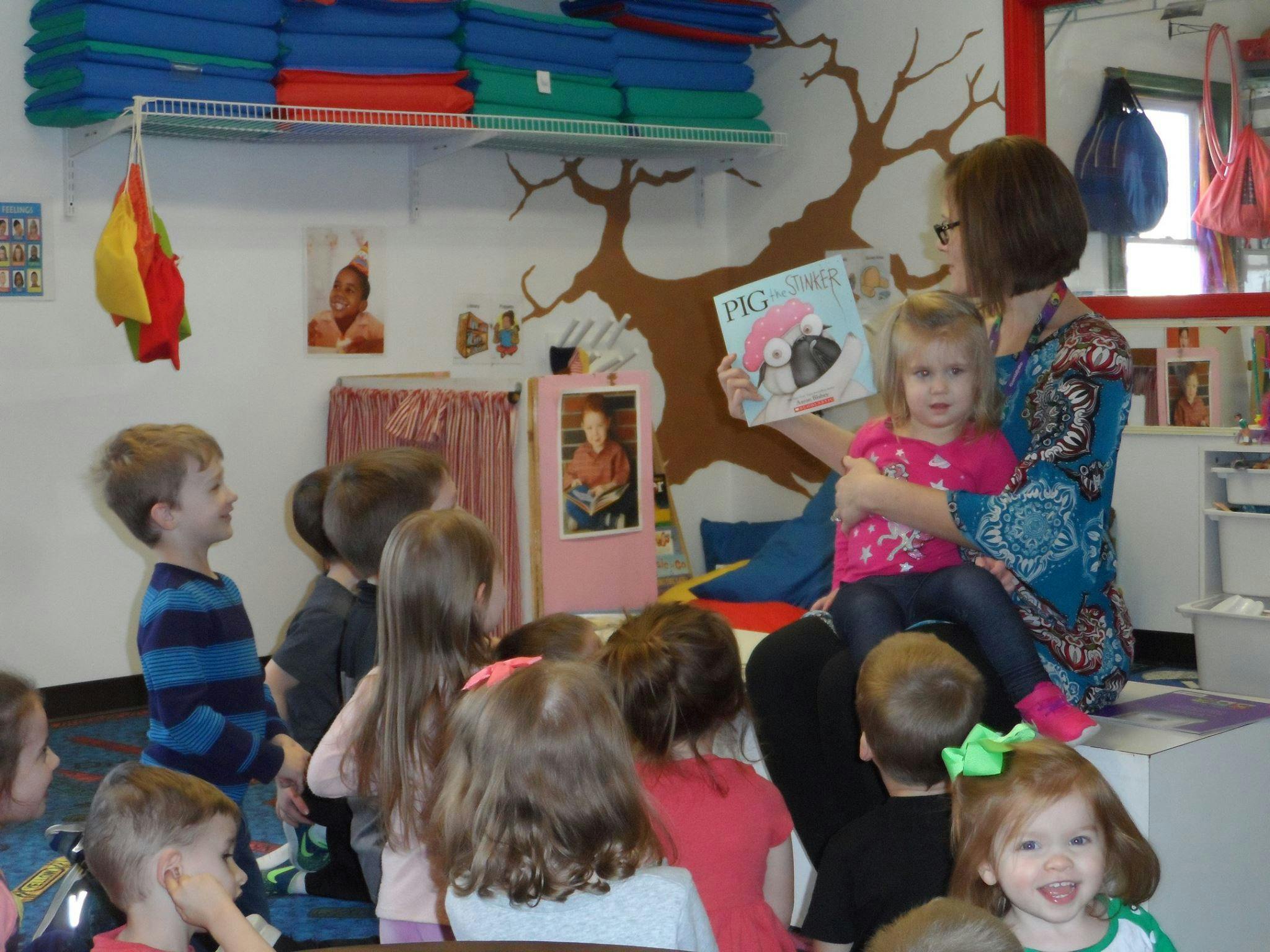 Person reading a book to a group of children in a classroom