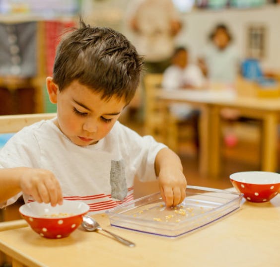 Child sorting small objects from a bowl into a tray in a classroom
