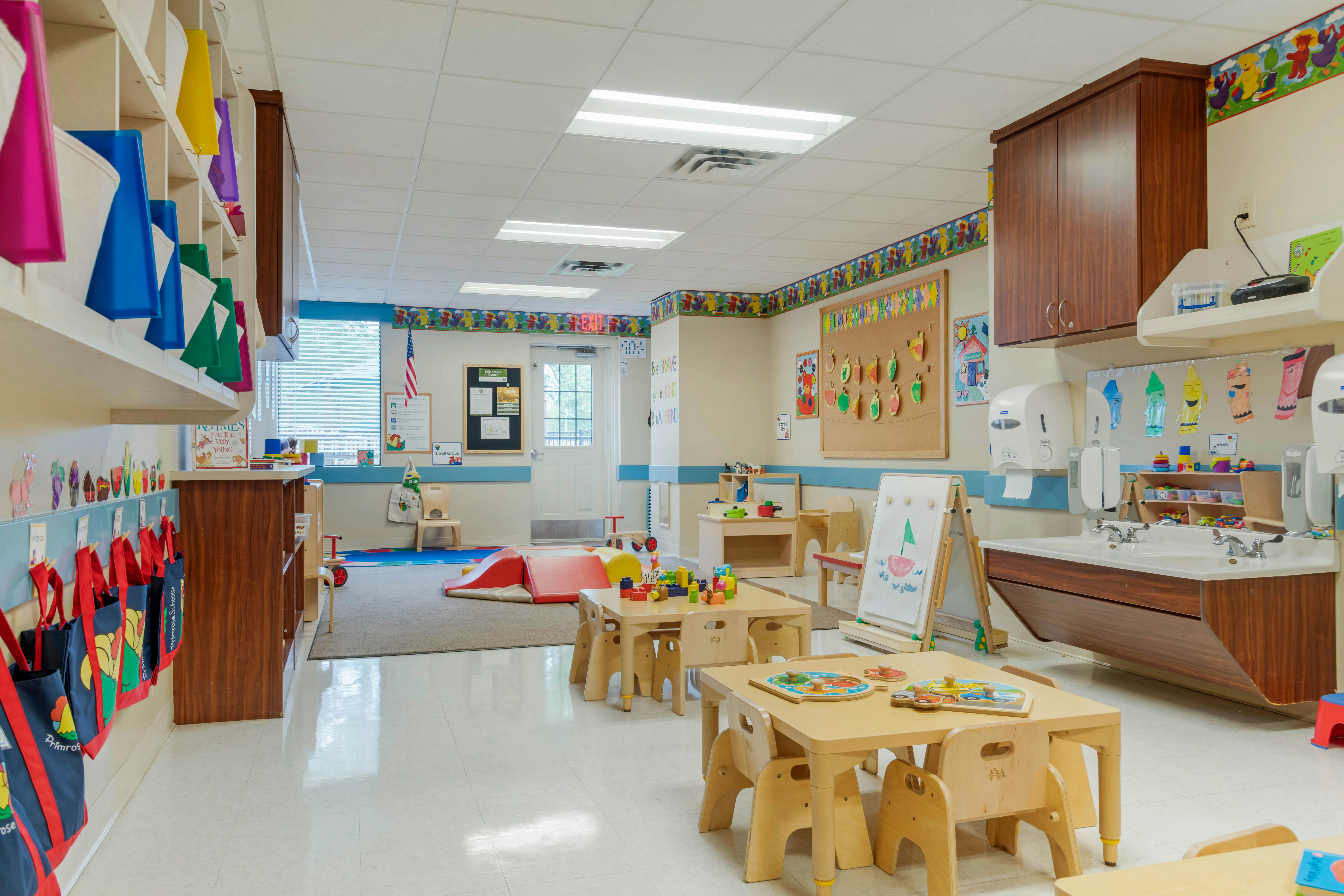 Classroom with small tables and chairs, play mats, and a double sink