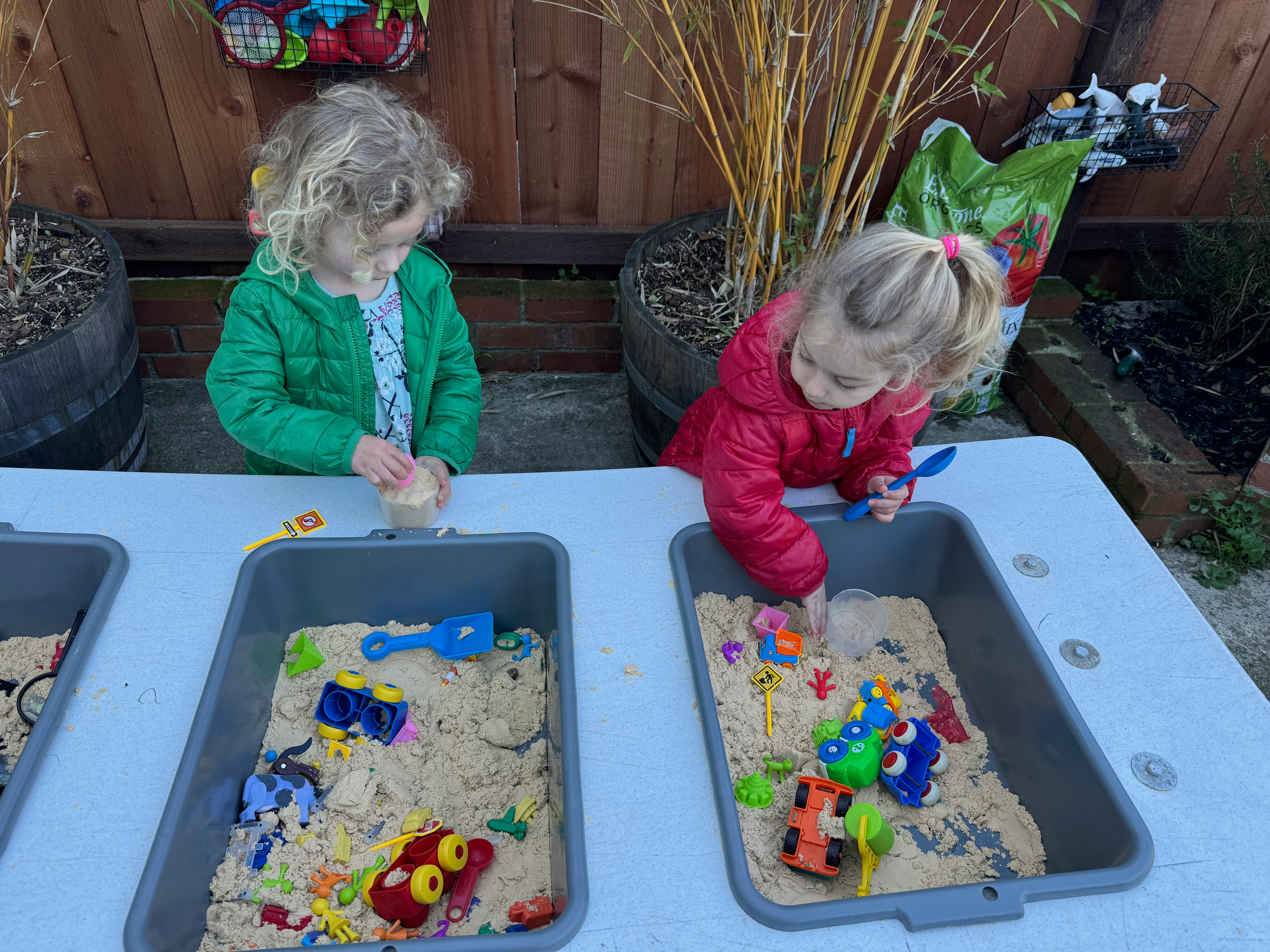 Two children playing with sand and toys in bins