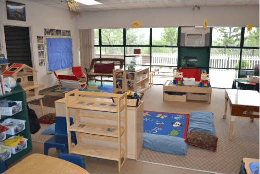 Classroom with various furniture and toys, large windows in background