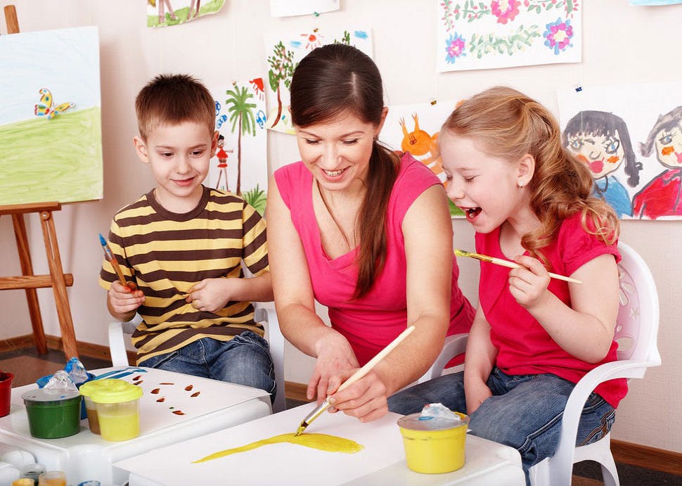 Person painting with two children in a classroom