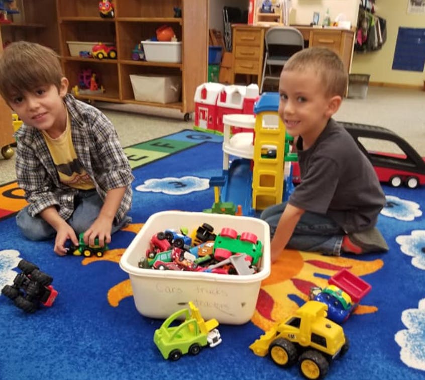 Two children playing with toy cars and a toy garage on a blue rug