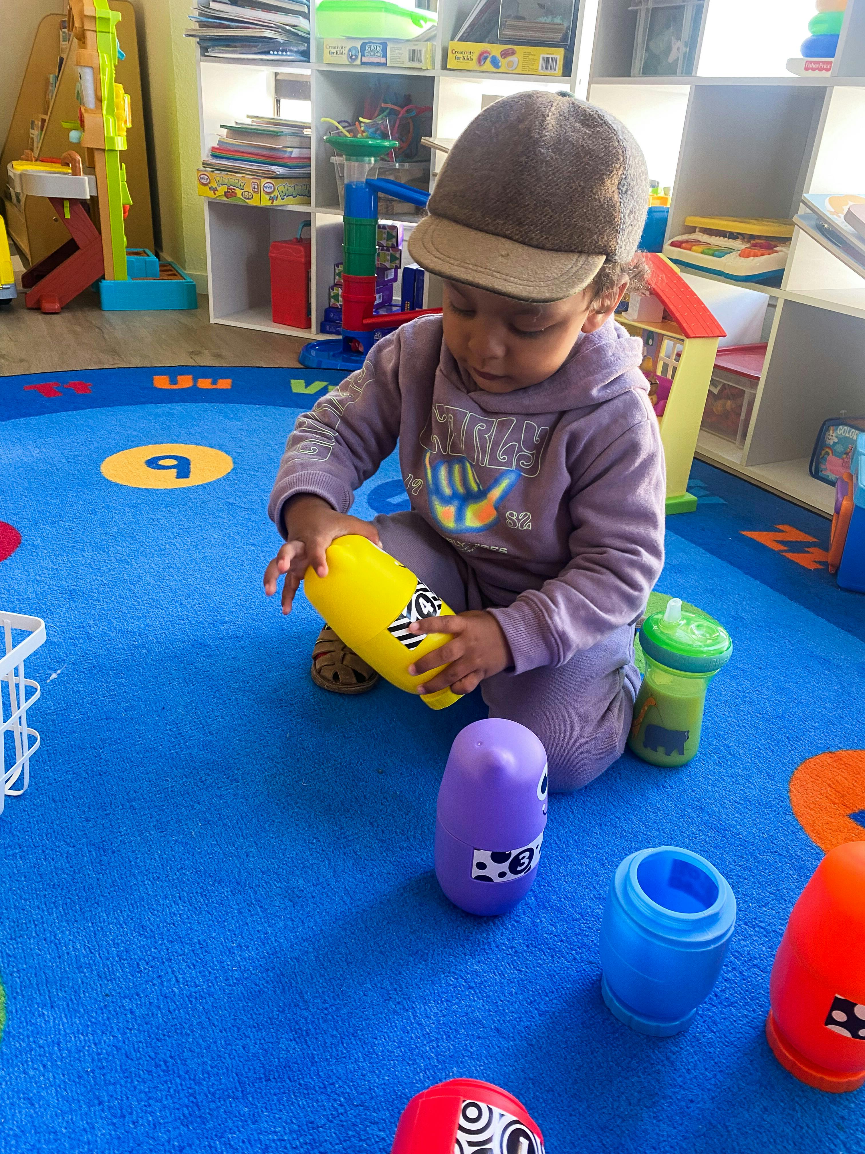 Child wearing a hat and purple clothes playing with toys on a blue rug