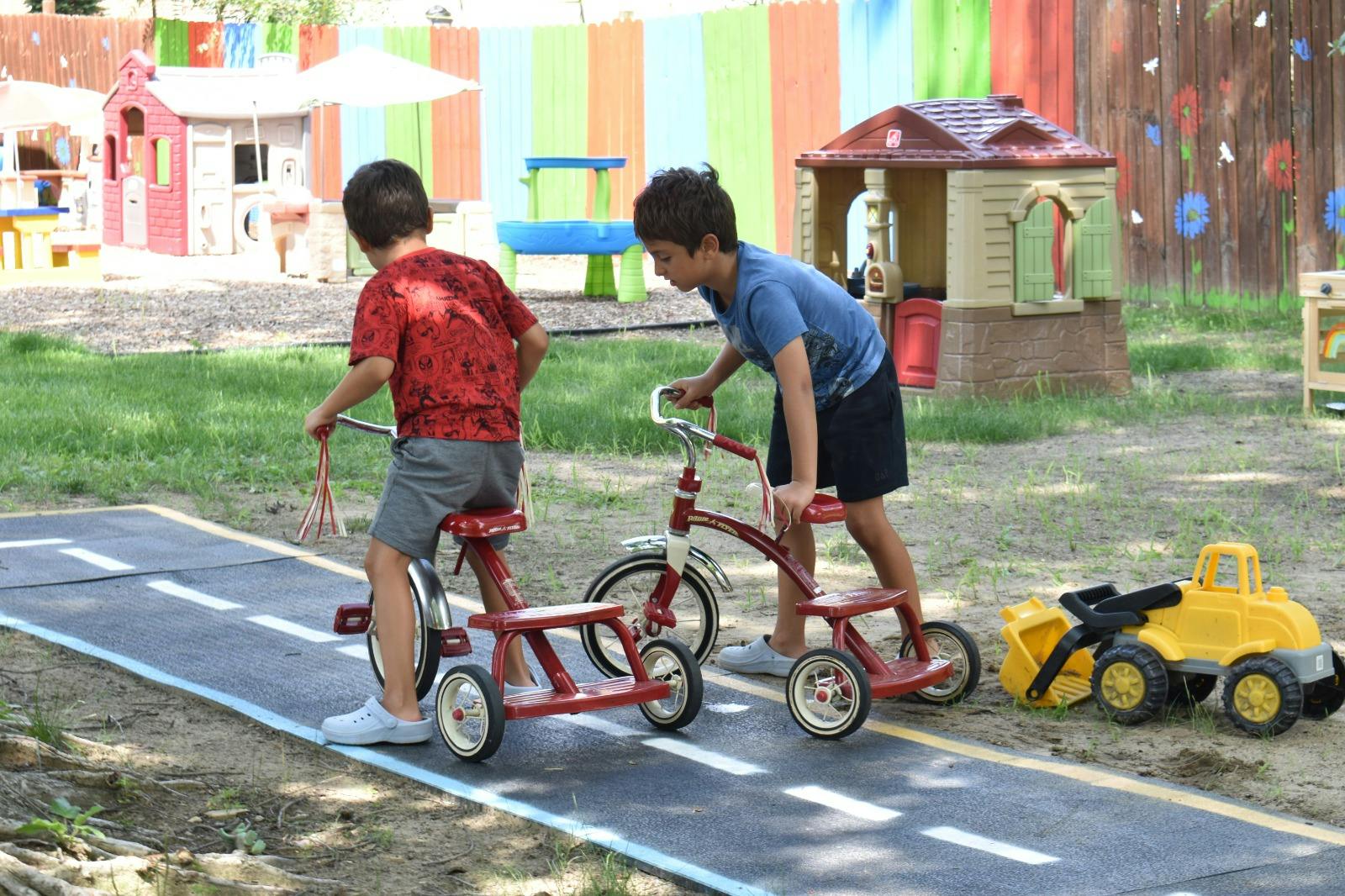 Two children playing with tricycles on a play track in a yard