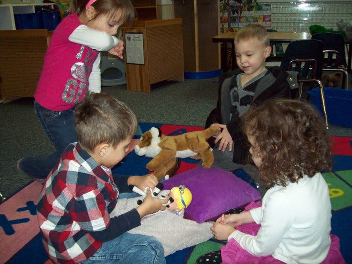 Four children playing with stuffed animals and toys on a rug