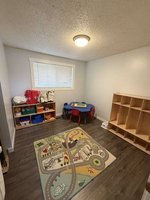 Playroom with a children's table, chairs, toy storage units, and a road rug