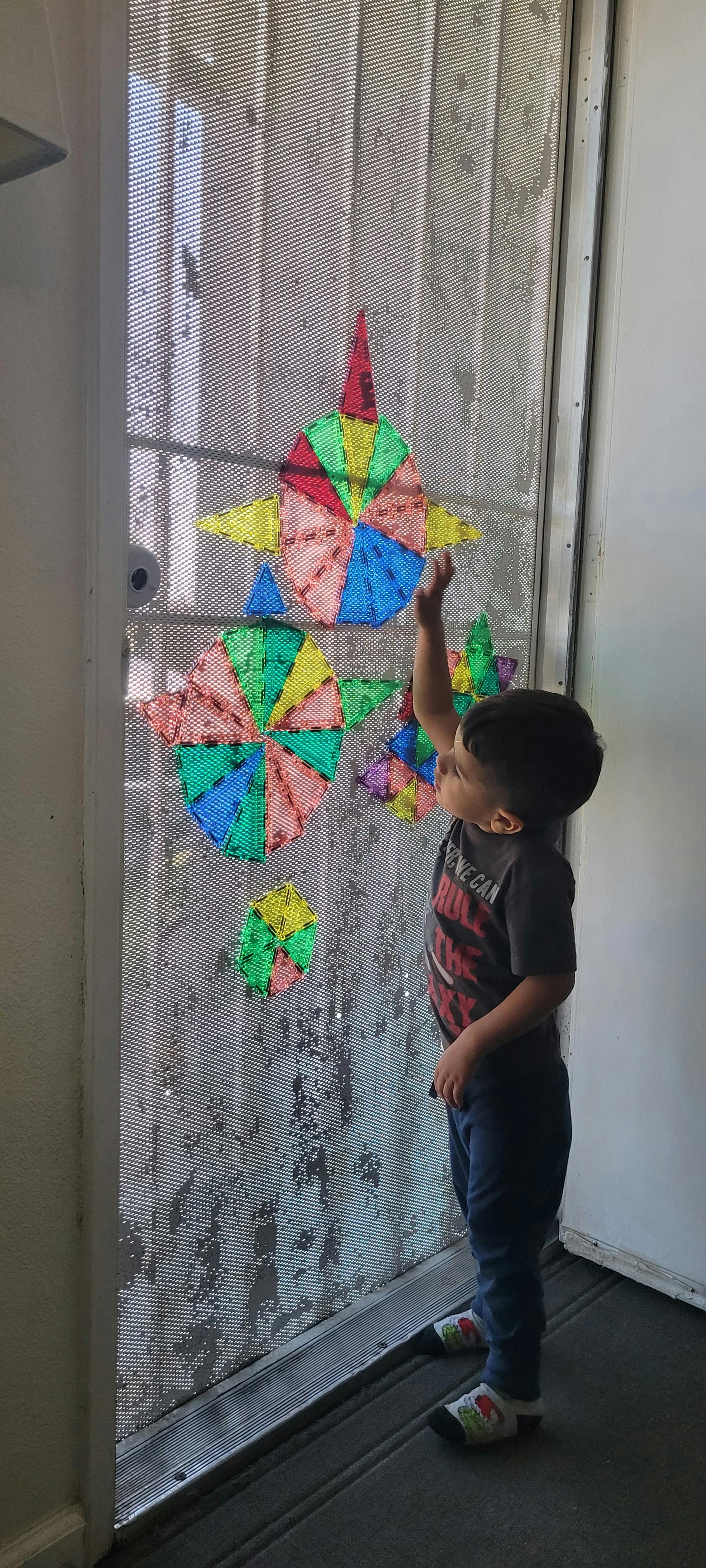 Child reaching up to colorful paper decorations on a screen door