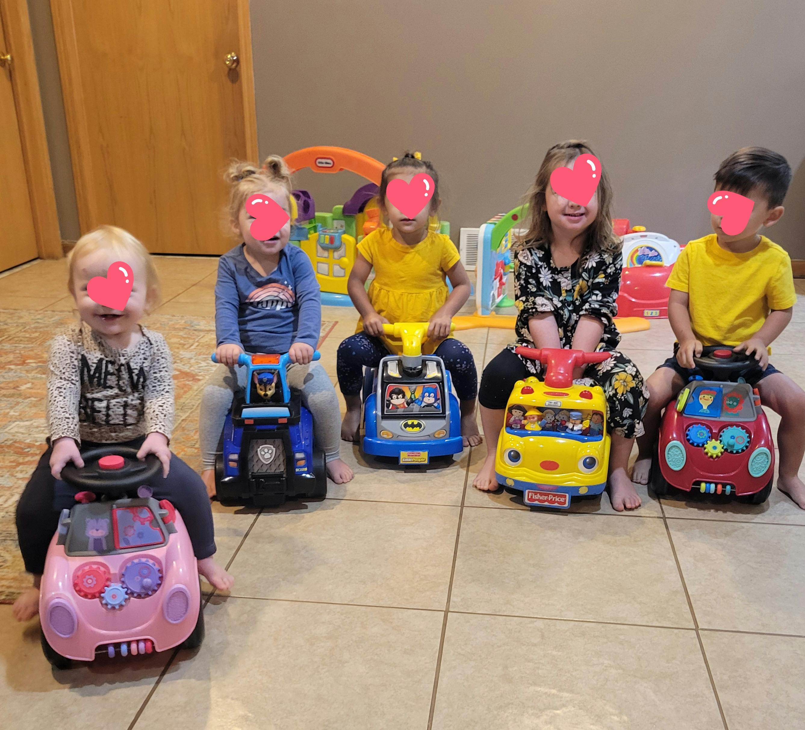 Five children sitting on ride-on toys indoors