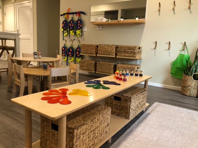 Classroom with small tables and chairs, storage baskets, and colorful shapes on a long table