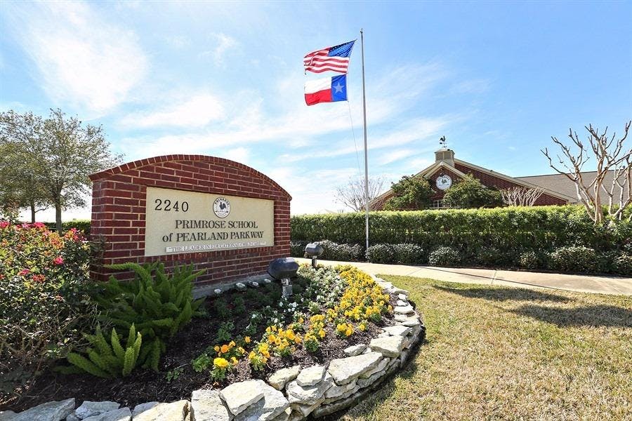 Brick sign for Primrose School of Pearland and Friends with flags flying