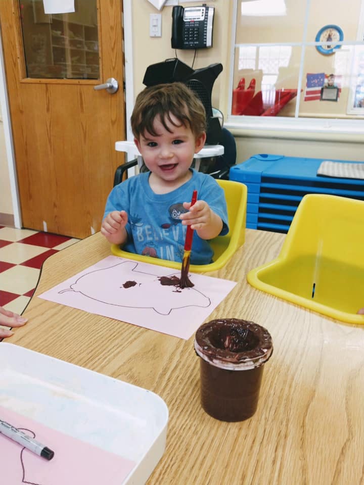 Child painting with brown paint in a classroom