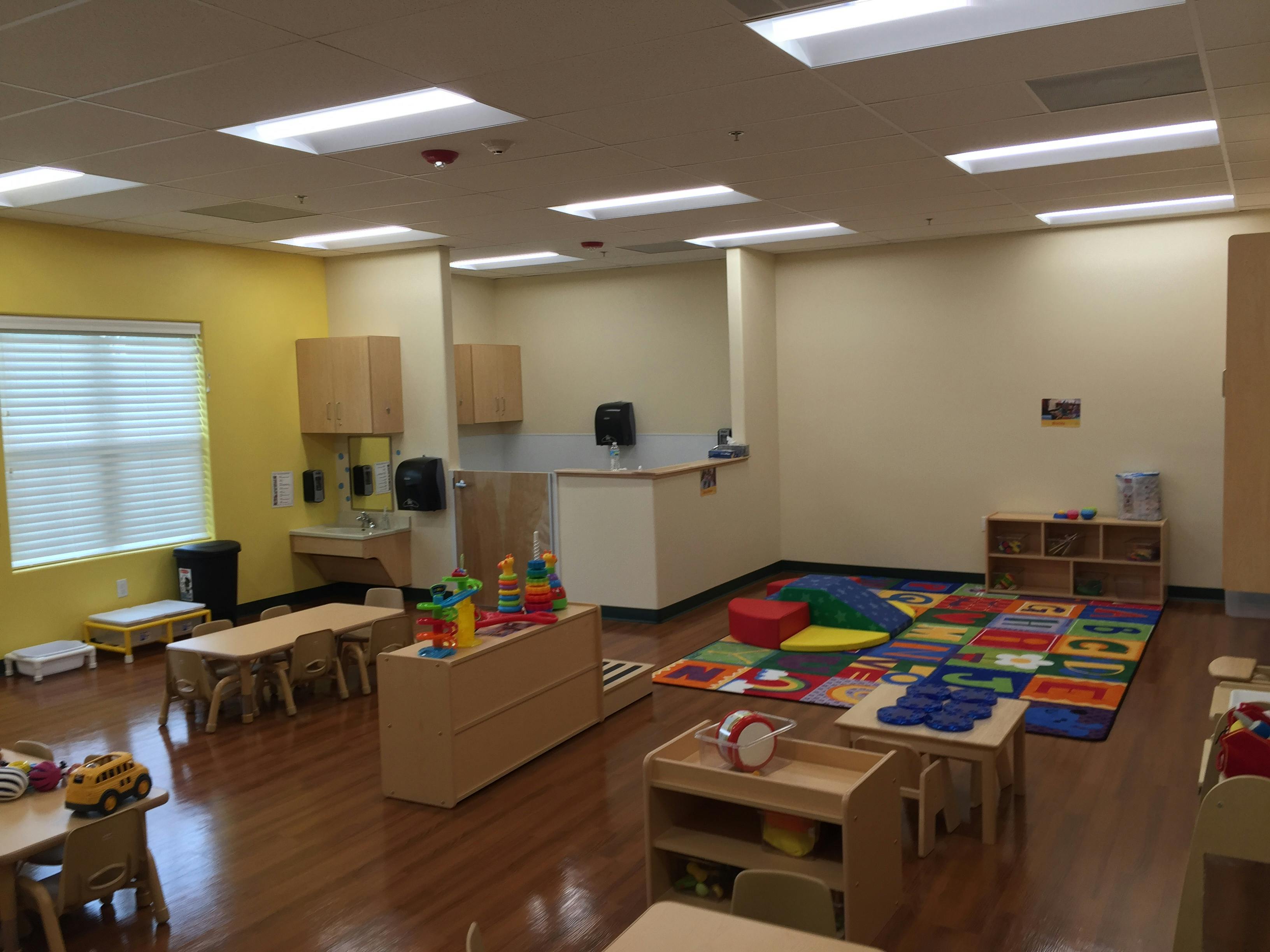Classroom with small tables, chairs, and a colorful play mat