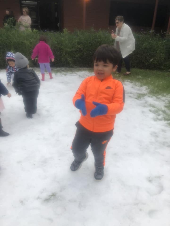 Child in orange jacket and blue gloves standing in snow