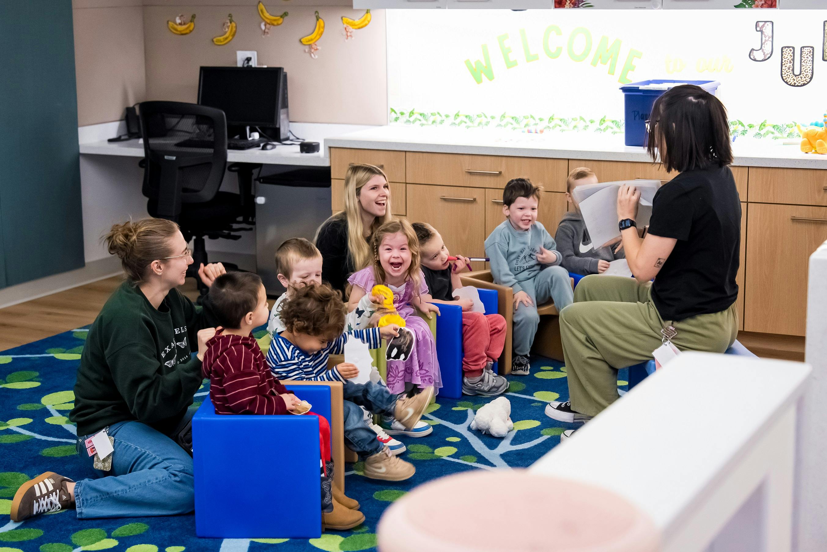 People in a classroom with an adult reading to a group of children