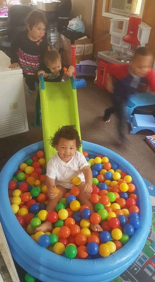 Child in a ball pit with a slide, other children nearby