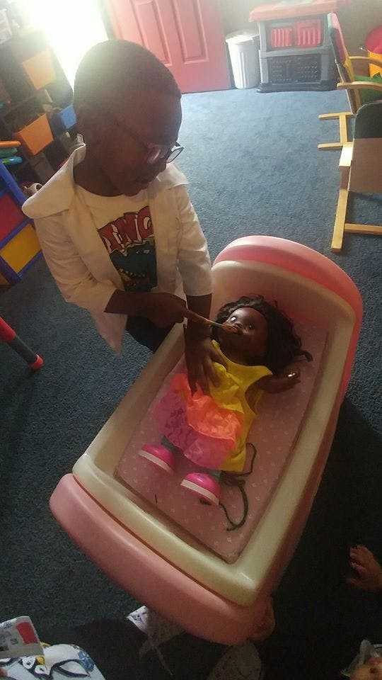 Child in glasses playing with a doll in a pink toy bed