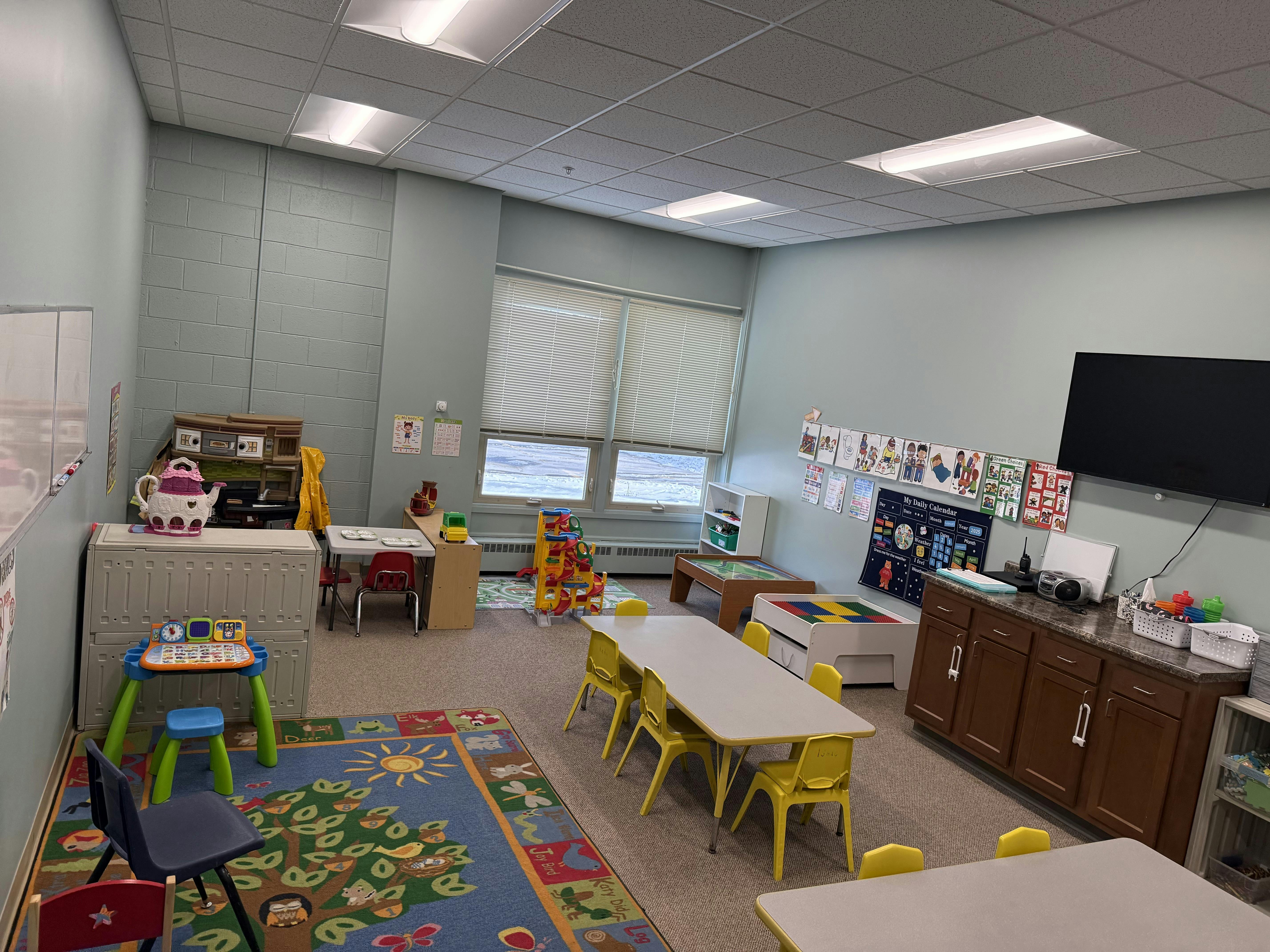 A classroom with child-sized tables and chairs, a play area, and learning materials