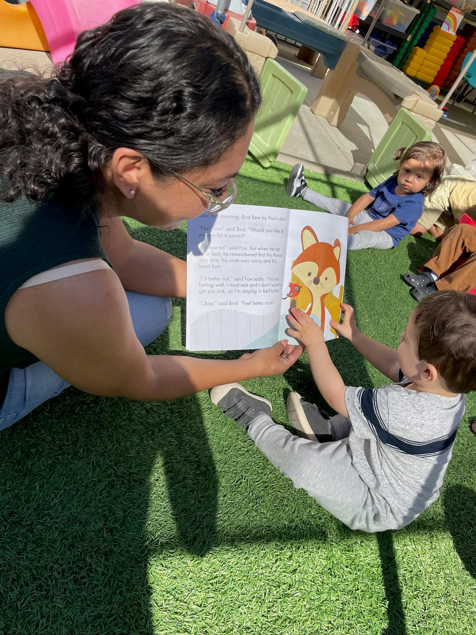Person reading a book with a child on artificial grass