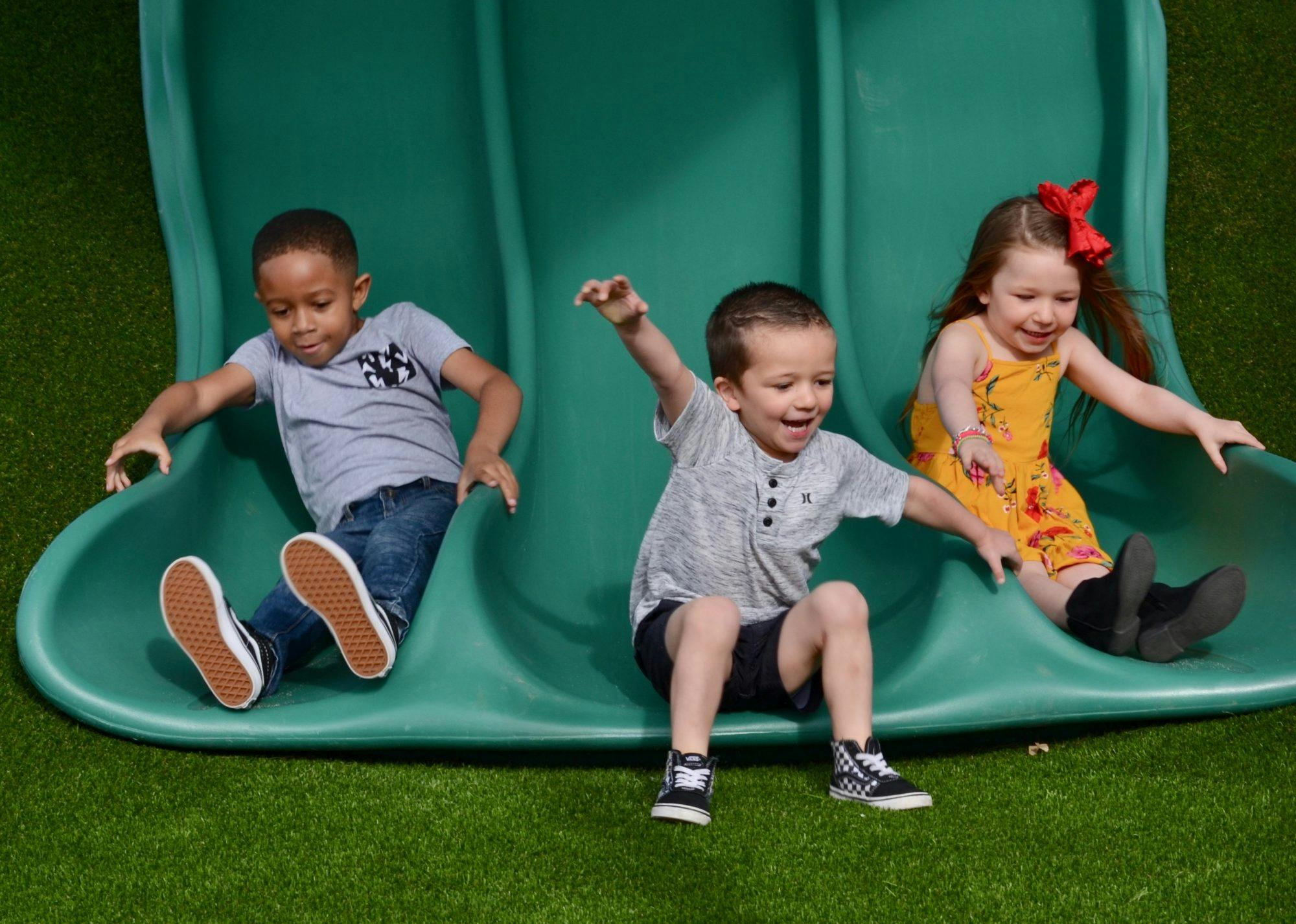Three children sliding down a green slide
