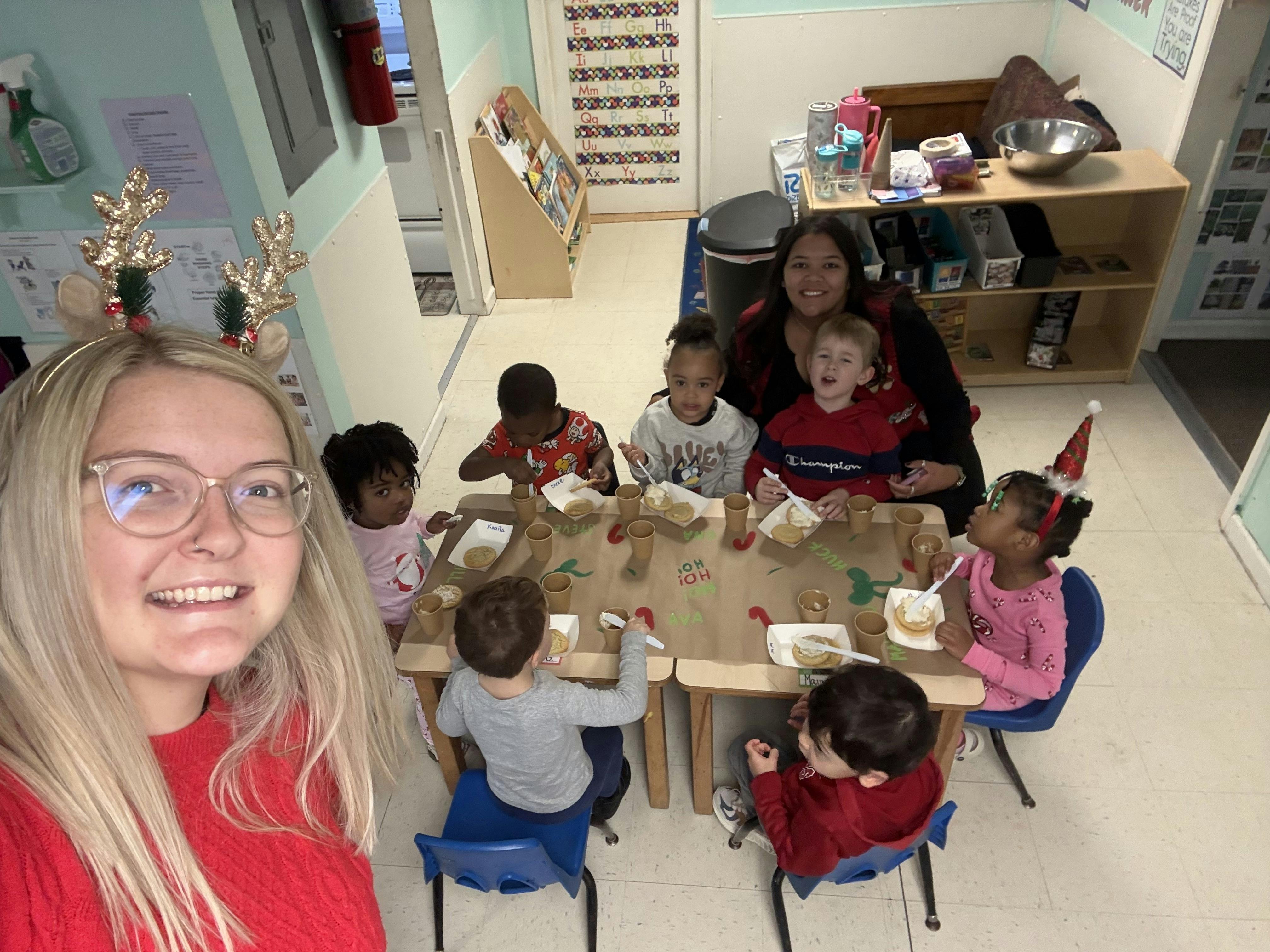 Teacher in reindeer antlers taking a selfie with children at a table