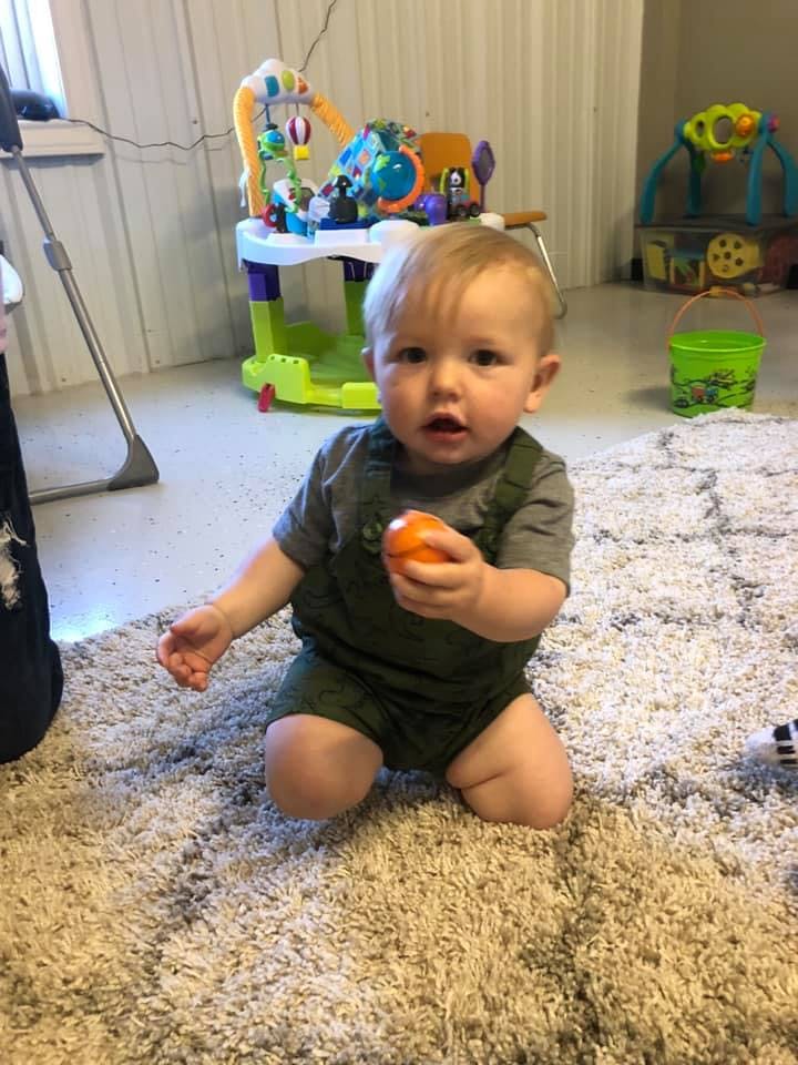 Child kneeling on a rug holding an orange toy