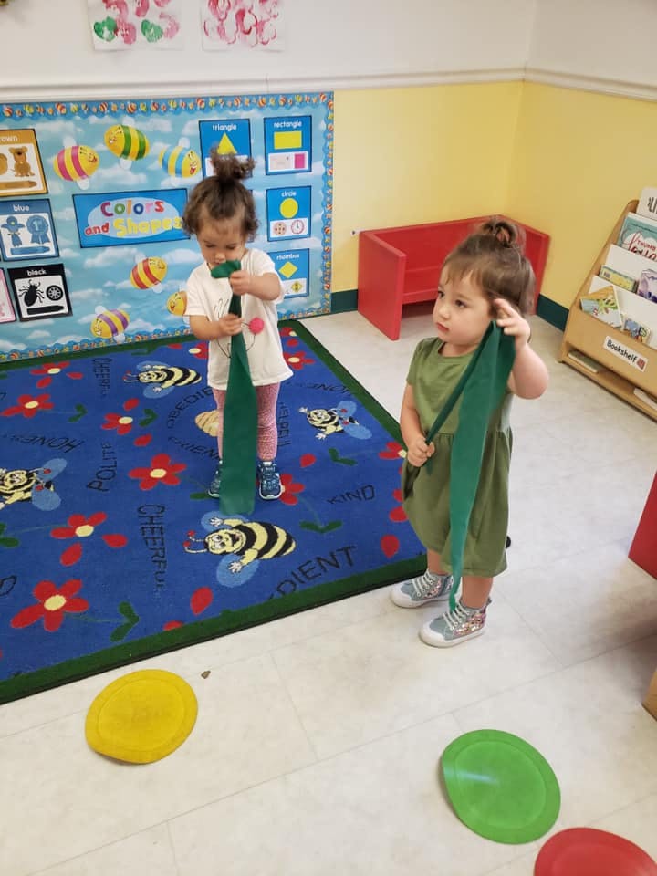 Two children holding green fabric strips in a classroom