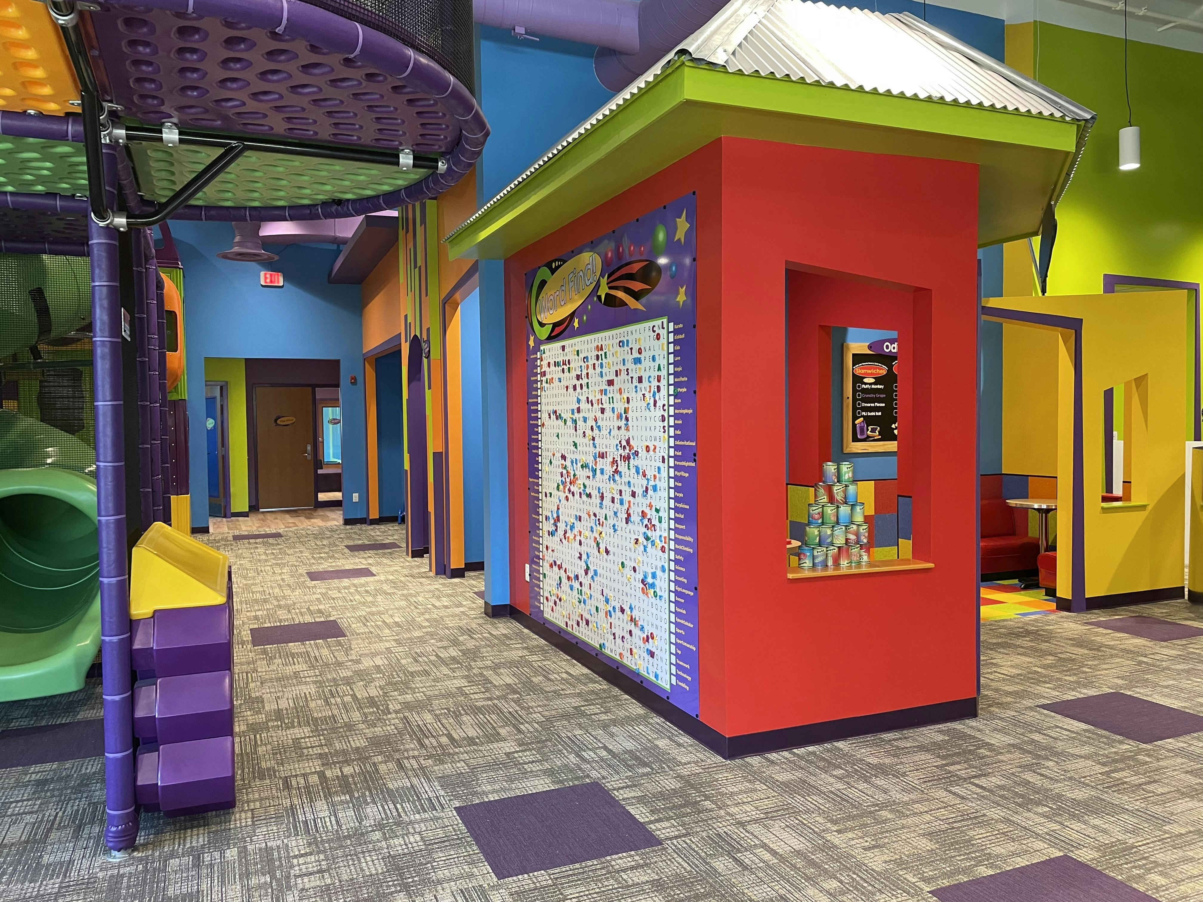 Colorful play area with a large word find board and a small red booth with canned goods