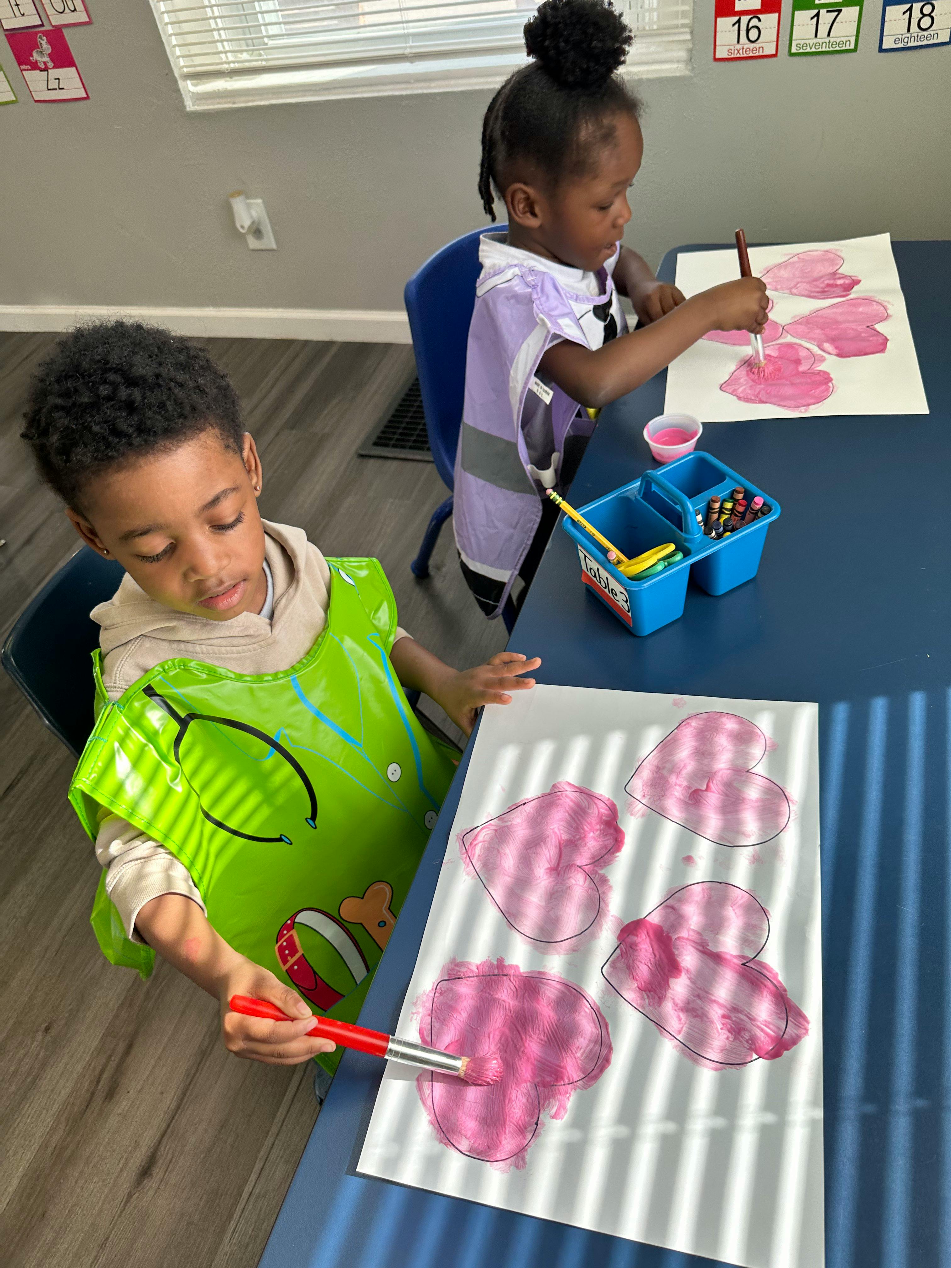 Two children painting heart shapes at a table