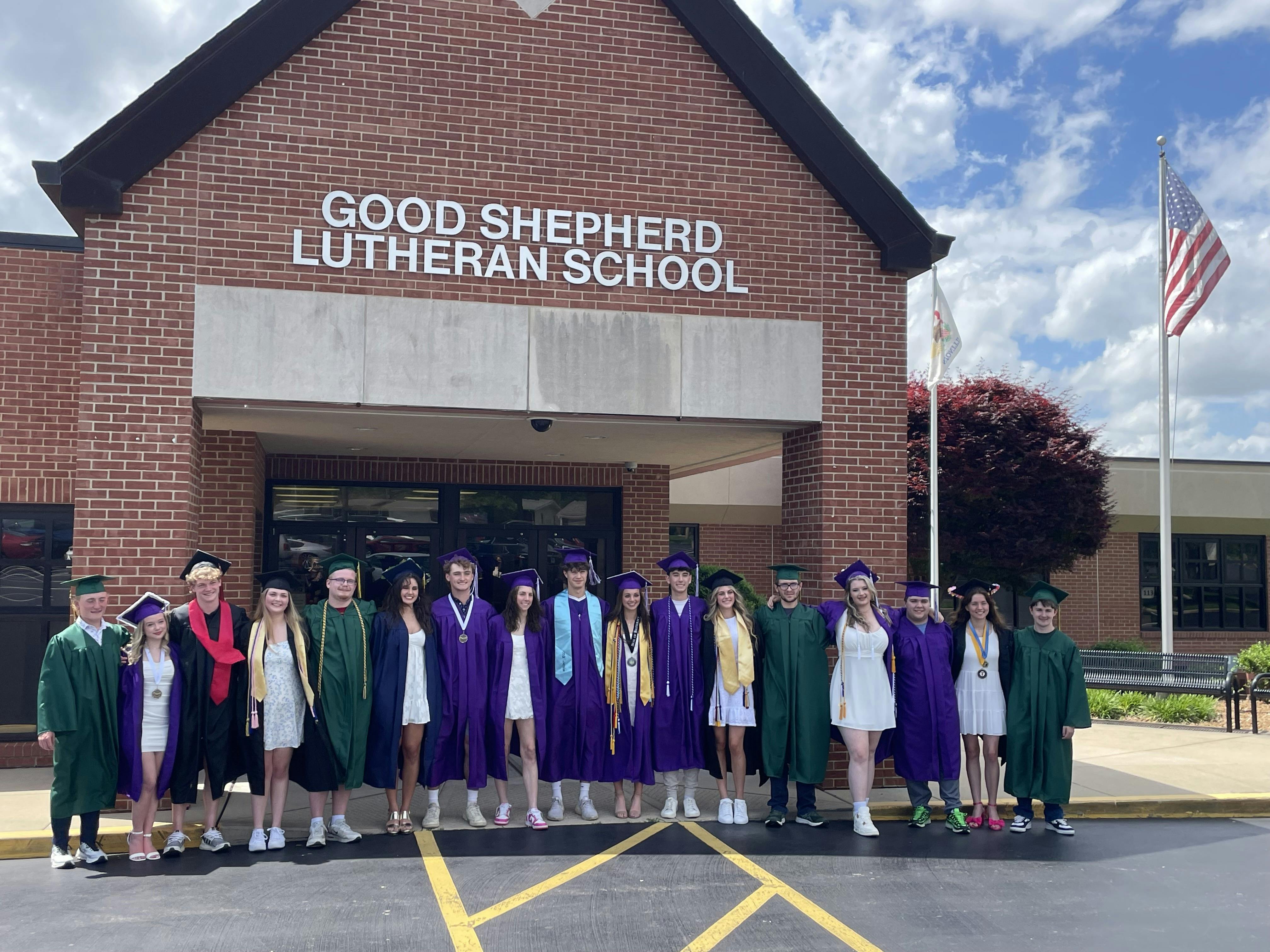 Group of students in graduation gowns standing in front of school building