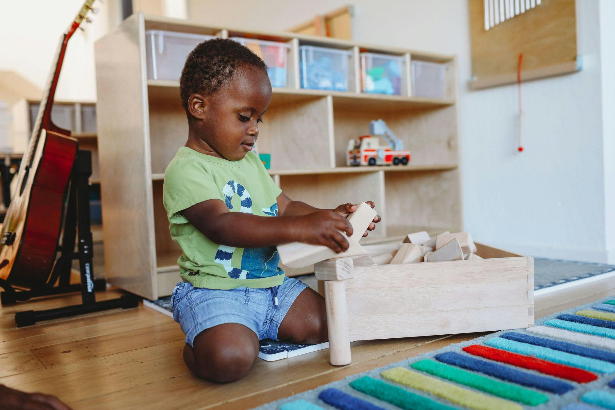 Child kneeling on floor playing with wooden blocks in a classroom