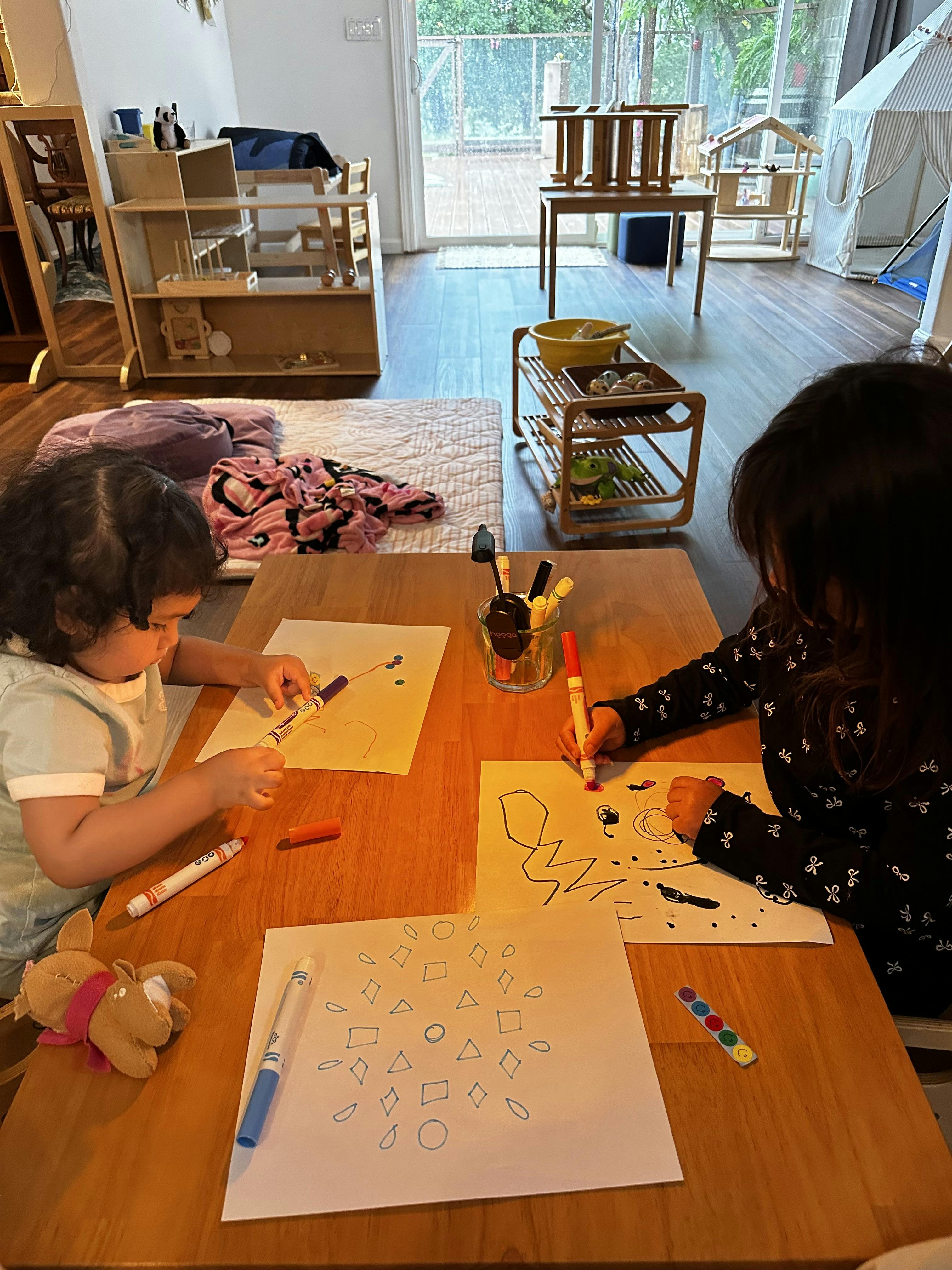 Two children sitting at a table drawing with markers