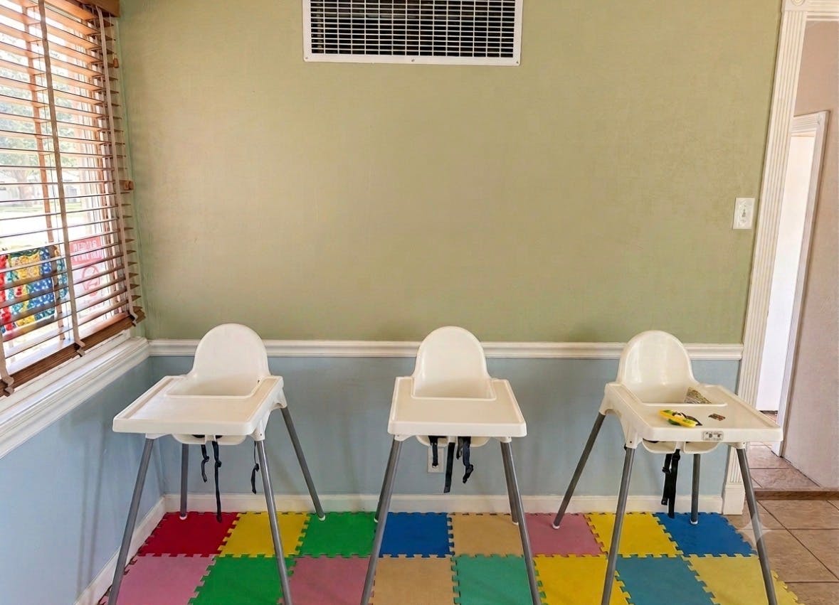 Three empty white high chairs on a colorful foam floor mat