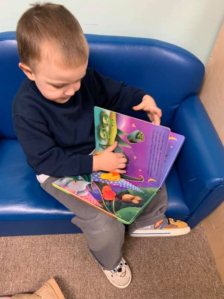Child sitting on a blue couch, looking at a colorful open book