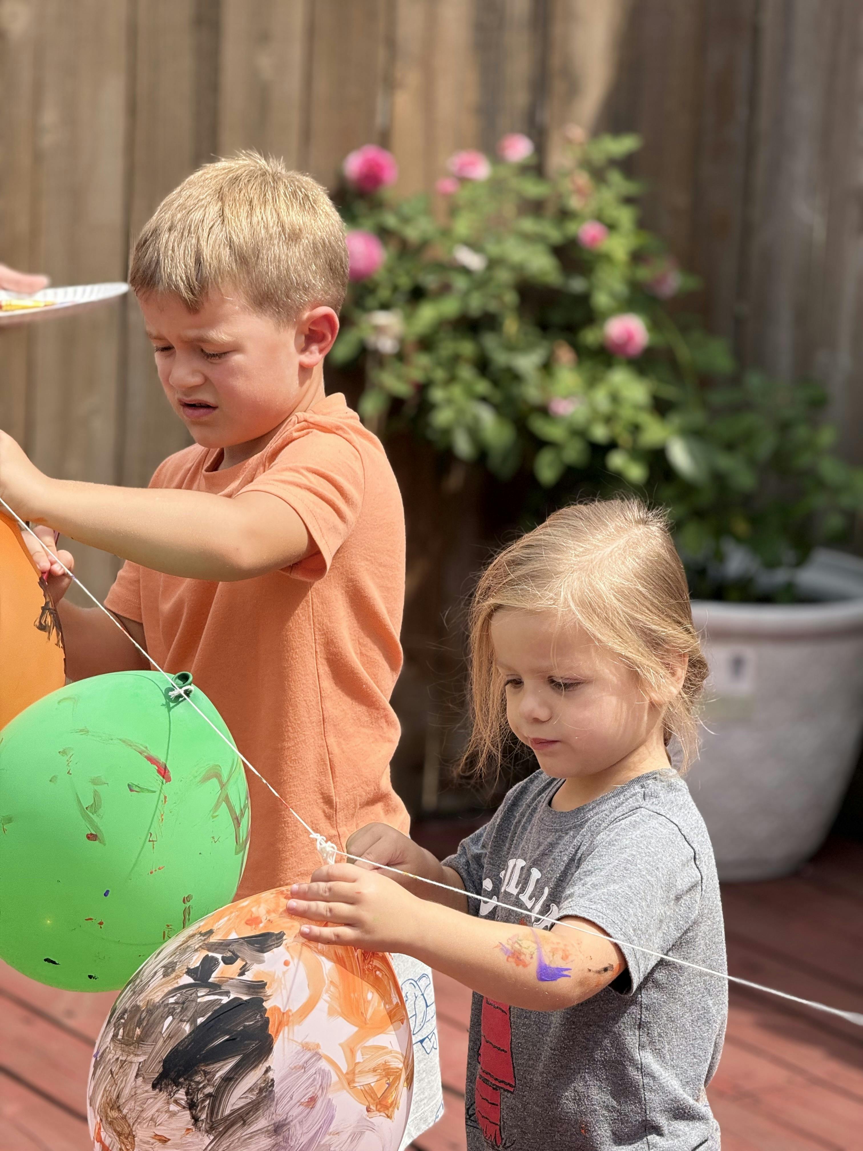 Two children playing with balloons on strings outdoors