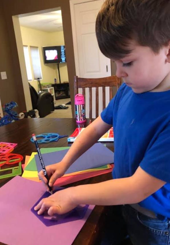 Child tracing a shape on purple paper with a pencil