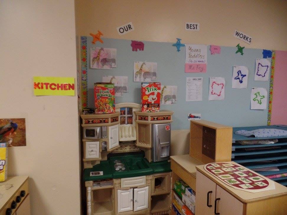 Play kitchen with toy food and a bulletin board with children's artwork