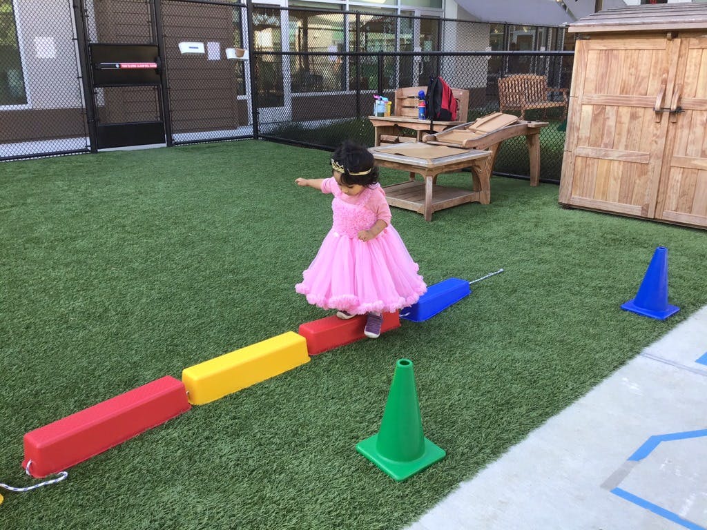 Child in pink dress walking on colorful balance beam