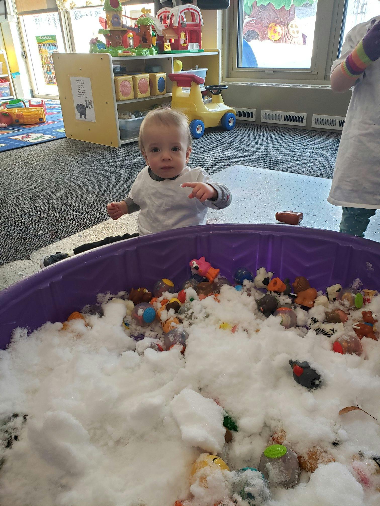 Child standing next to a purple bin filled with white foam and toys