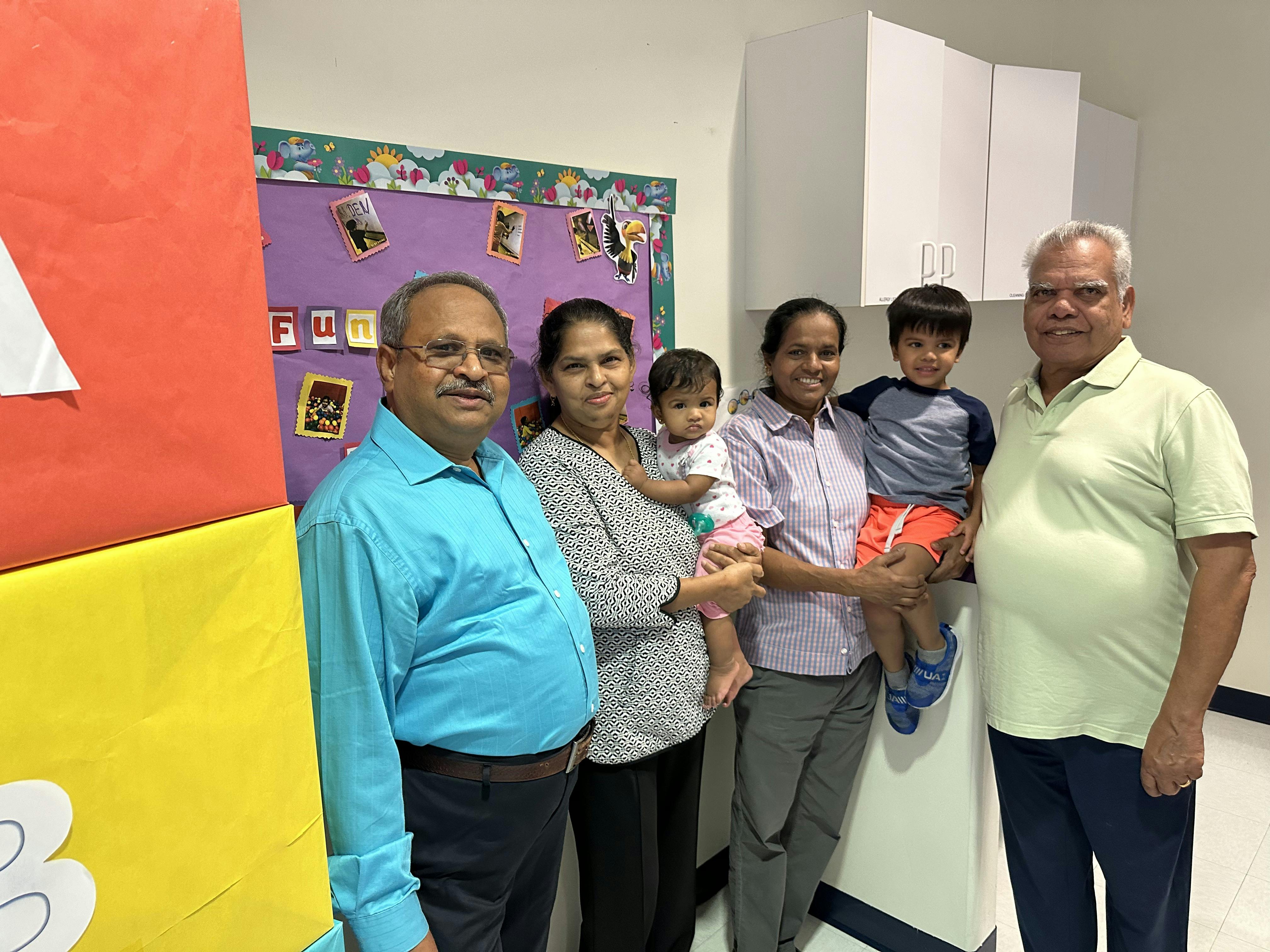 Five adults and two children posing for a group photo indoors