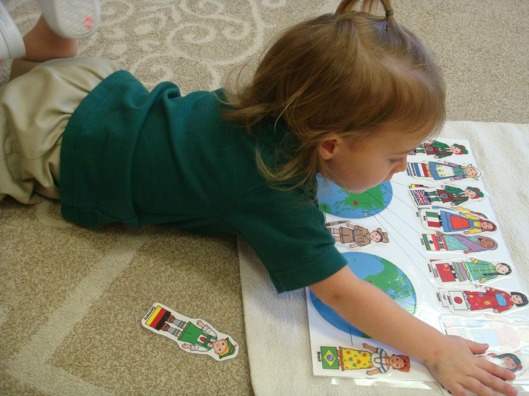 Child lying on floor playing with a puzzle of people from around the world