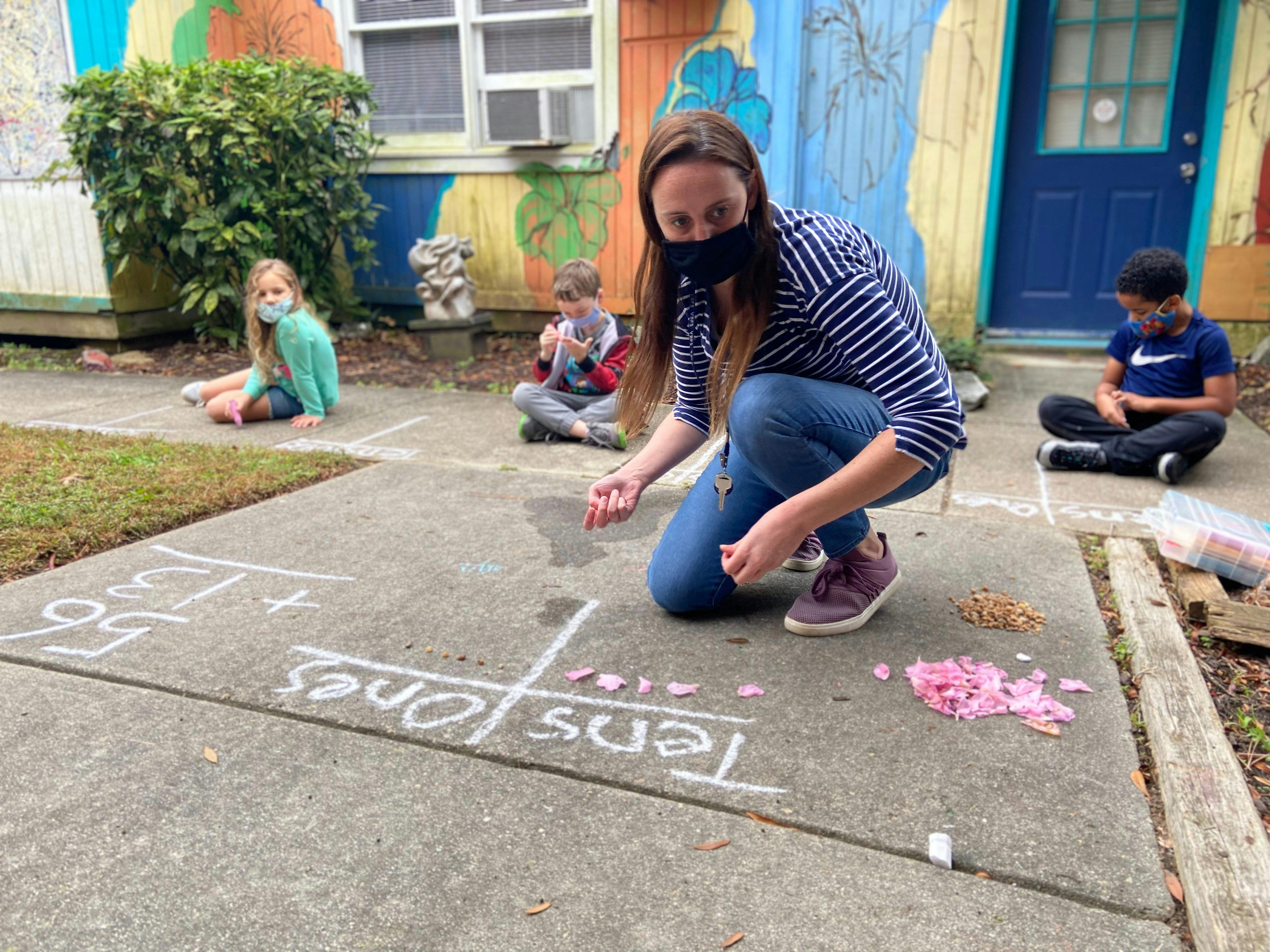 Person kneeling on sidewalk with children, chalk math problem on ground